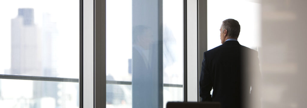 Middle-aged businessman staring out of the window of a modern office structure whilst considering why CIOs are choosing Managed IT for strategic freedom