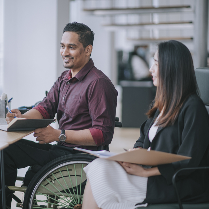 A person in a wheelchair sat next to another person at a desk viewing a digital screen illustrating how managed IT services are helping not-for-profit organisations benefit from tech adoption